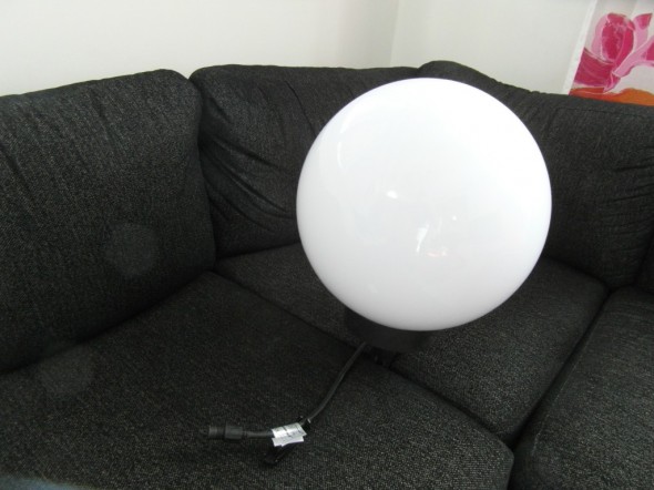Iso valkoinen pallovalaisin "istutettuna" sohvatyynyjen väliin. Kokoluokka hahmottuu tästä ehkä vähäsen?